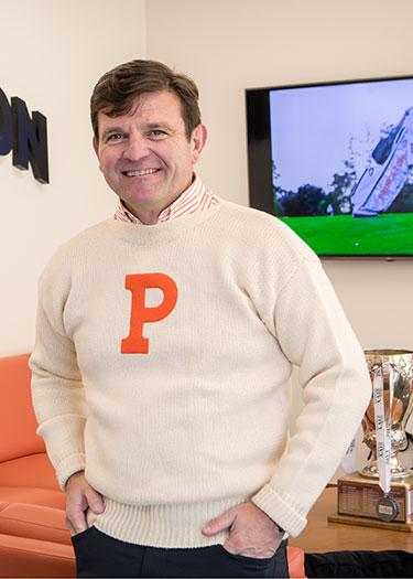 A man in a white sweater with an orange letter P on it smiles