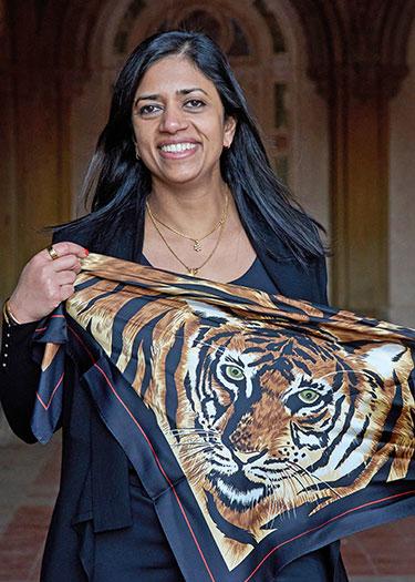 A woman holding a scarf with a tiger image on it smiles